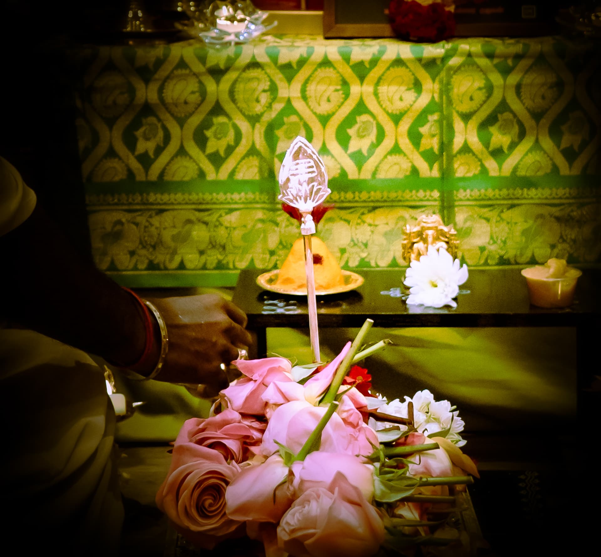 A sacred Vel surrounded by pink flowers before a green ceremonial backdrop